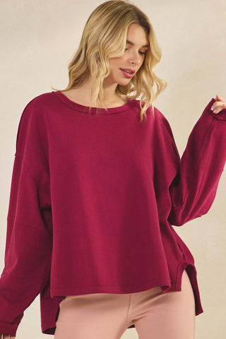 A woman wearing a burgundy, relaxed fit top with long sleeves and a crew neckline.