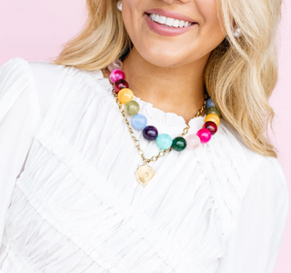 Necklace with colorful round beads and a gold-toned pendant worn over a white blouse.