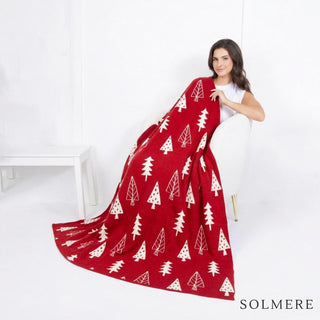 A red blanket with white Christmas tree motifs draped over a chair.