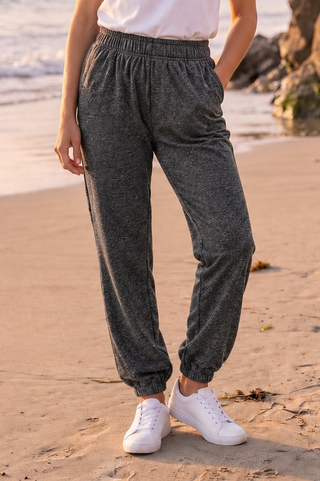 Black relaxed-fit joggers with elastic waistband and cuffs, worn on a beach.