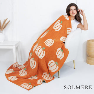 A cozy orange blanket with animated pumpkin print draped over a chair.