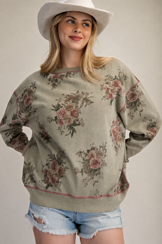 Woman wearing a green olive pullover with floral print, styled with denim shorts and a white hat.