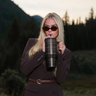 A 40 oz tumbler with a flannel pattern design held by a person outdoors.
