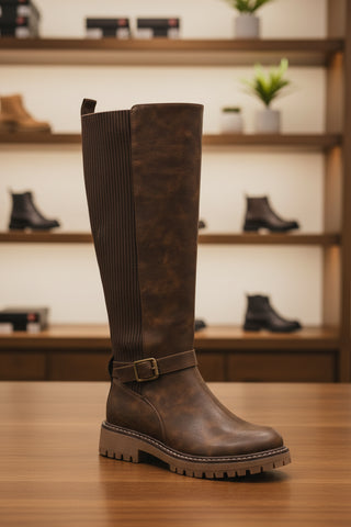 Mocha slip-on flats with a cushioned footbed and rounded toe, placed on a wooden surface in a shoe store.