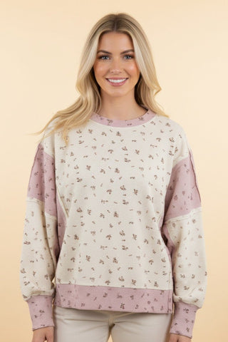 A woman wearing a cream waffle knit sweatshirt with a floral print, paired with jeans.