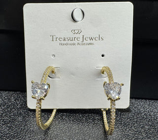 Gold hoop earrings with a heart-shaped crystal centerpiece on a display card.