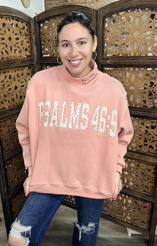 A woman wearing a pink mockneck top with 'Psalms 46' printed on it.