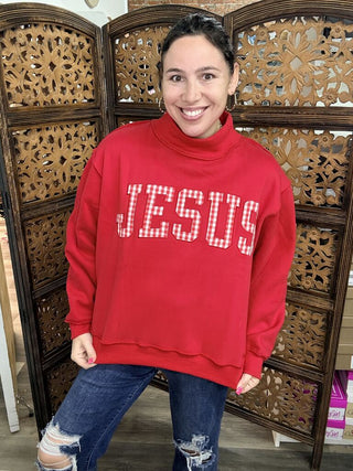 Red sweatshirt with 'Jesus' print and a turtleneck, worn by a person.