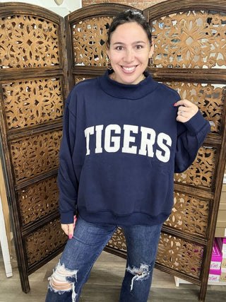 Navy sweatshirt with 'TIGERS' print and mock neck, worn by a person indoors.