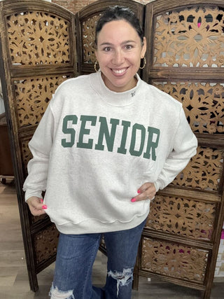 A person wearing a heather gray sweatshirt with 'Senior' printed in green.