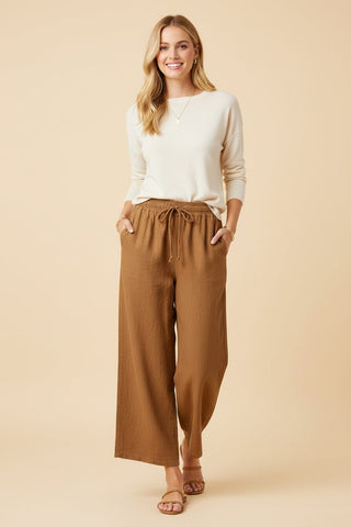 A woman wearing taupe high-rise wide-leg pants with a drawstring waist and pockets.