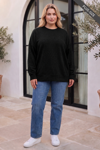 A plus-size model wearing a black long-sleeve sweater with a relaxed fit and crew neckline.