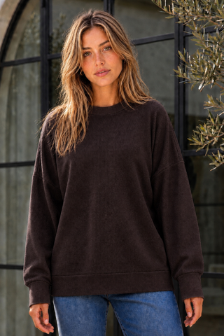 A woman wearing a relaxed fit coffee-colored sweatshirt with long sleeves.